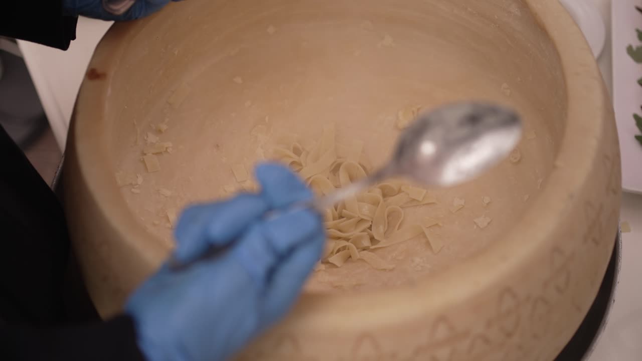 Fresh pasta being prepared inside a large cheese wheel, with utensils in hand