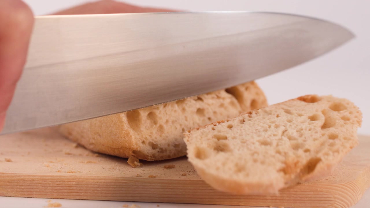 Person Slicing Fresh Crusty Bread on a Wooden Cutting Board