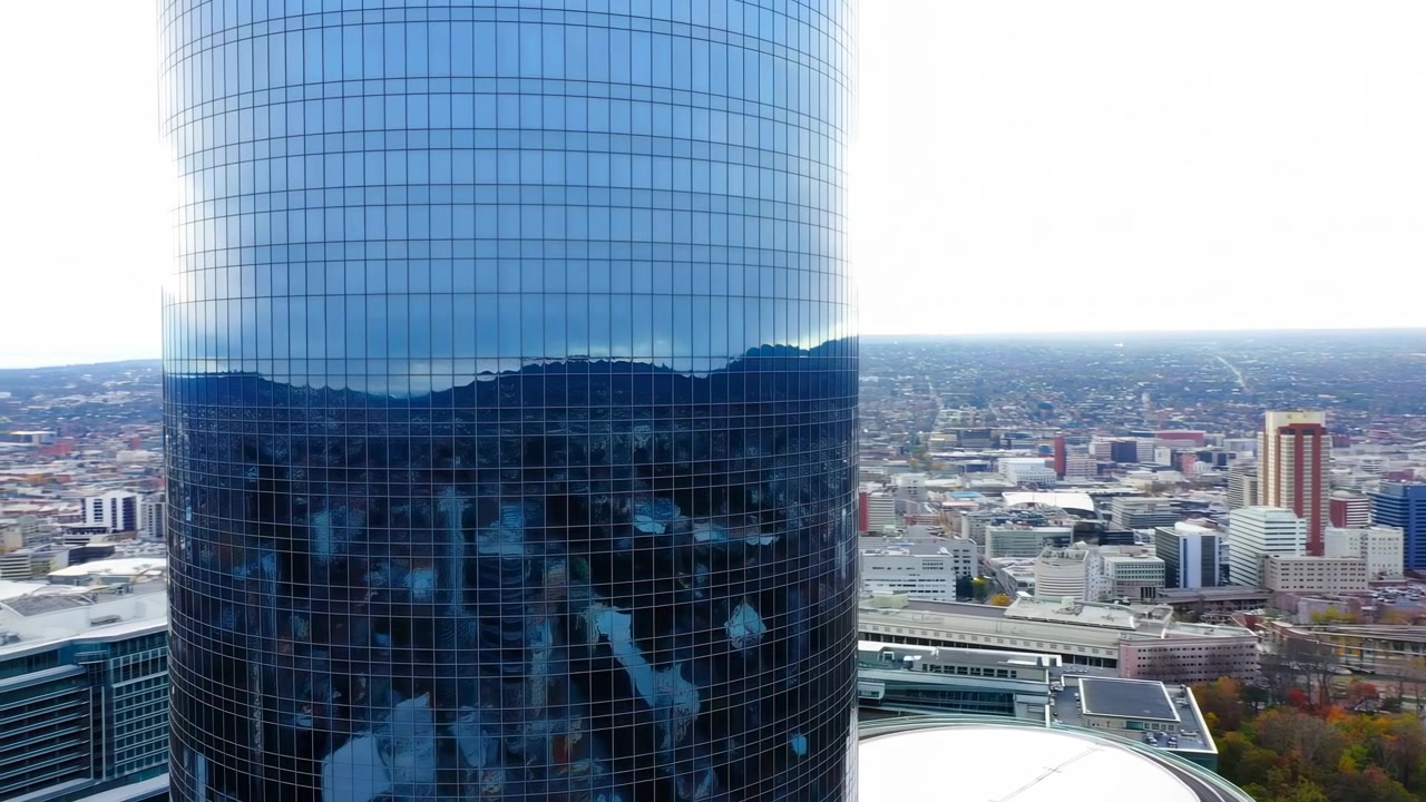 Luftaufnahme einer ruhigen urbanen Skyline mit Wolkenkratzern und Bergen im Hintergrund, Materialien aus Glas, Beton, Metall, blaue, graue, grüne, braune Farben, statische Ansicht, Stadtbild mit Wolkenkratzern.