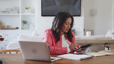 Middle-aged-African-American-woman-sitting-at-a-table-using-a-tablet-computer-and-stylus,-panning-shot