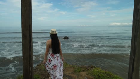 woman walking to precipice facing the sea _drone shot