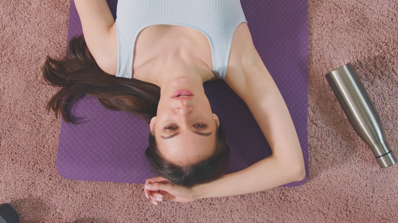 Ripresa dall'alto di una donna che si riposa su un tappetino da ginnastica a casa dopo l'allenamento - filmato al rallentatore.