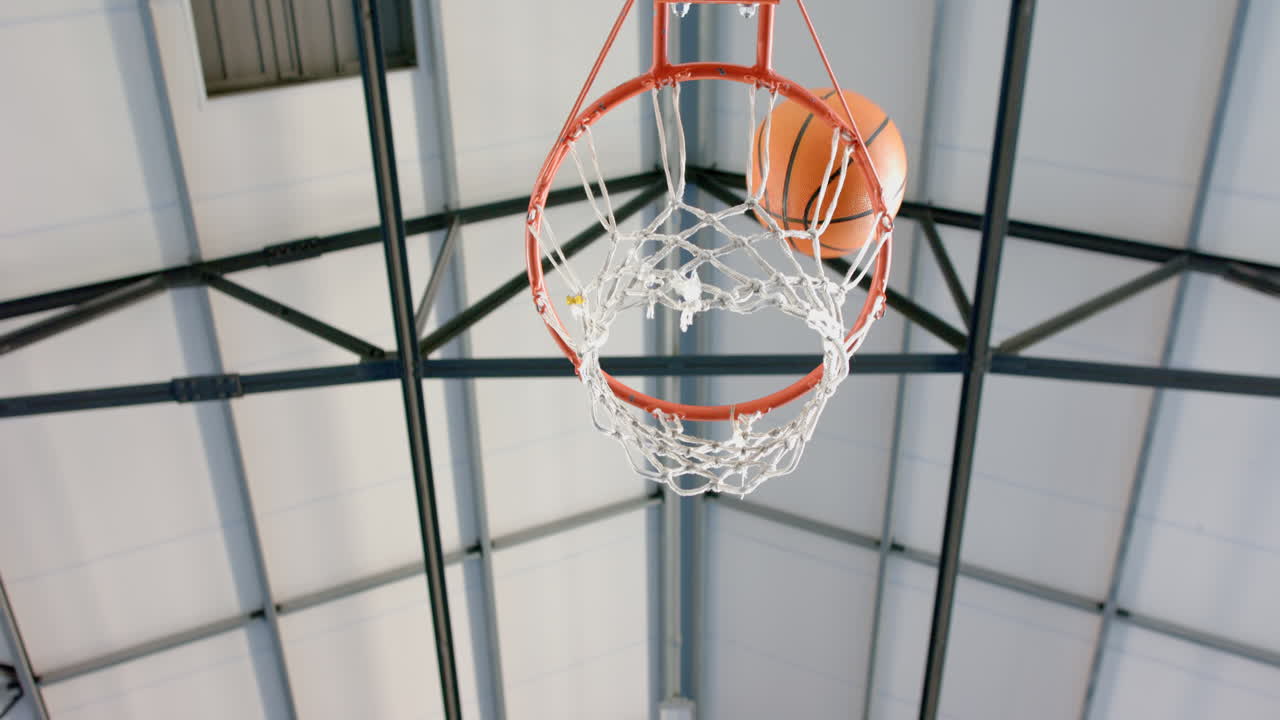 Scoring point, basketball going through hoop in indoor gym, copy space