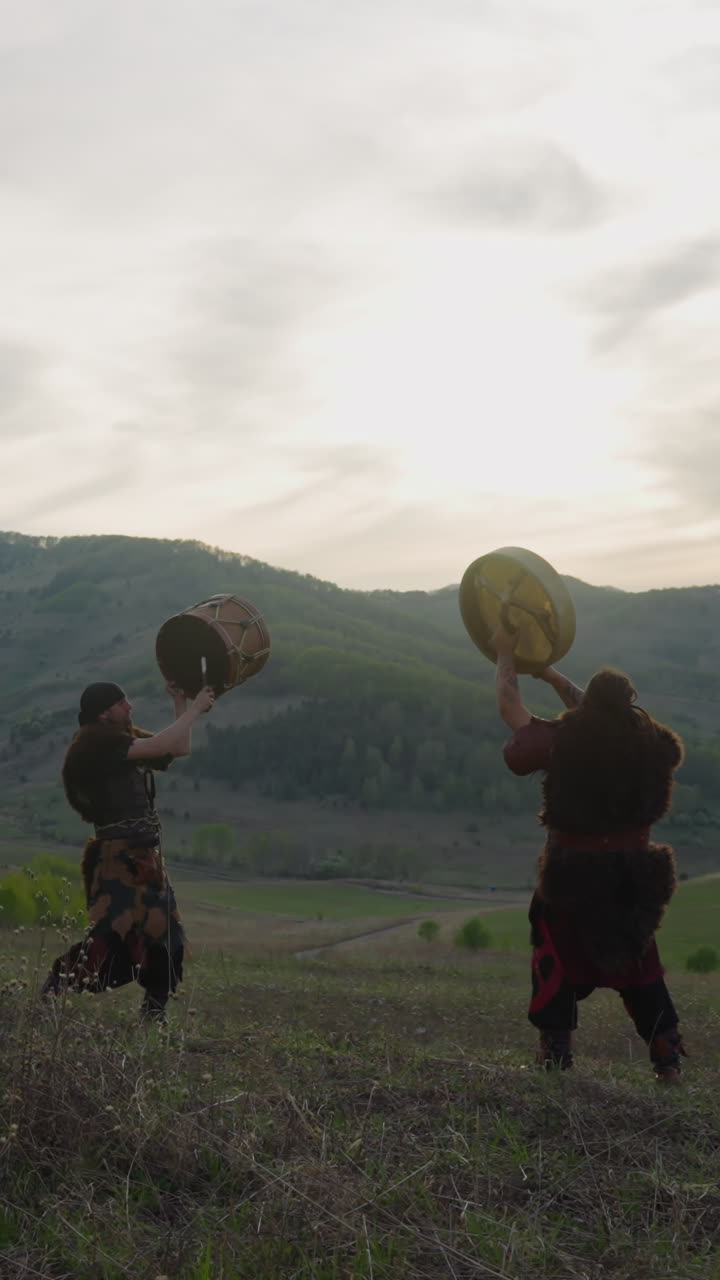 Couple of men wearing traditional Altai clothes conducts fertility ritual with drums in valley. Musicians supports folk spiritual traditions