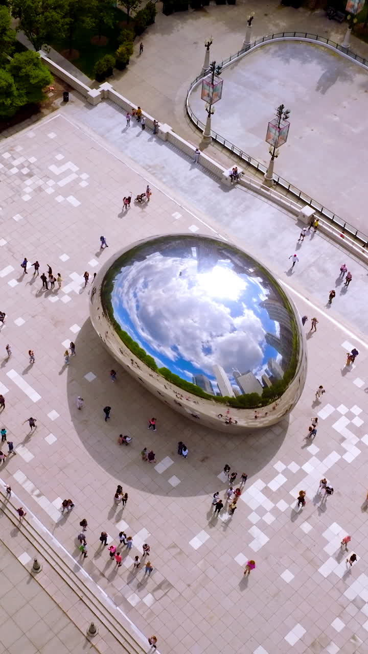 Iconic Cloud Gate surrounded by numerous tourists visiting the site. Top view on the blue cloudy sky reflecting in the big shining Bean. Vertical video
