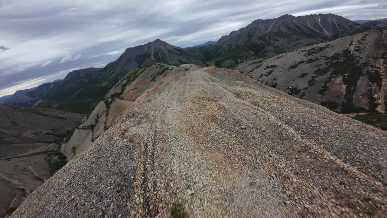Hikers traverse a rugged trail atop a mountain ridge, overlooking distant peaks and valleys