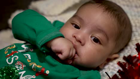 adorable y lindo bebé indio con una parte superior navideña festiva verde chupando la mano izquierda mientras se acuesta en una manta
