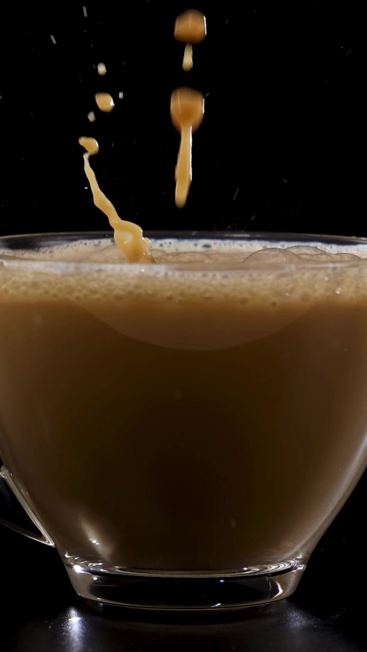 Il latte viene versato in una tazza da caffè di vetro, creando un effetto vorticoso su uno sfondo scuro.