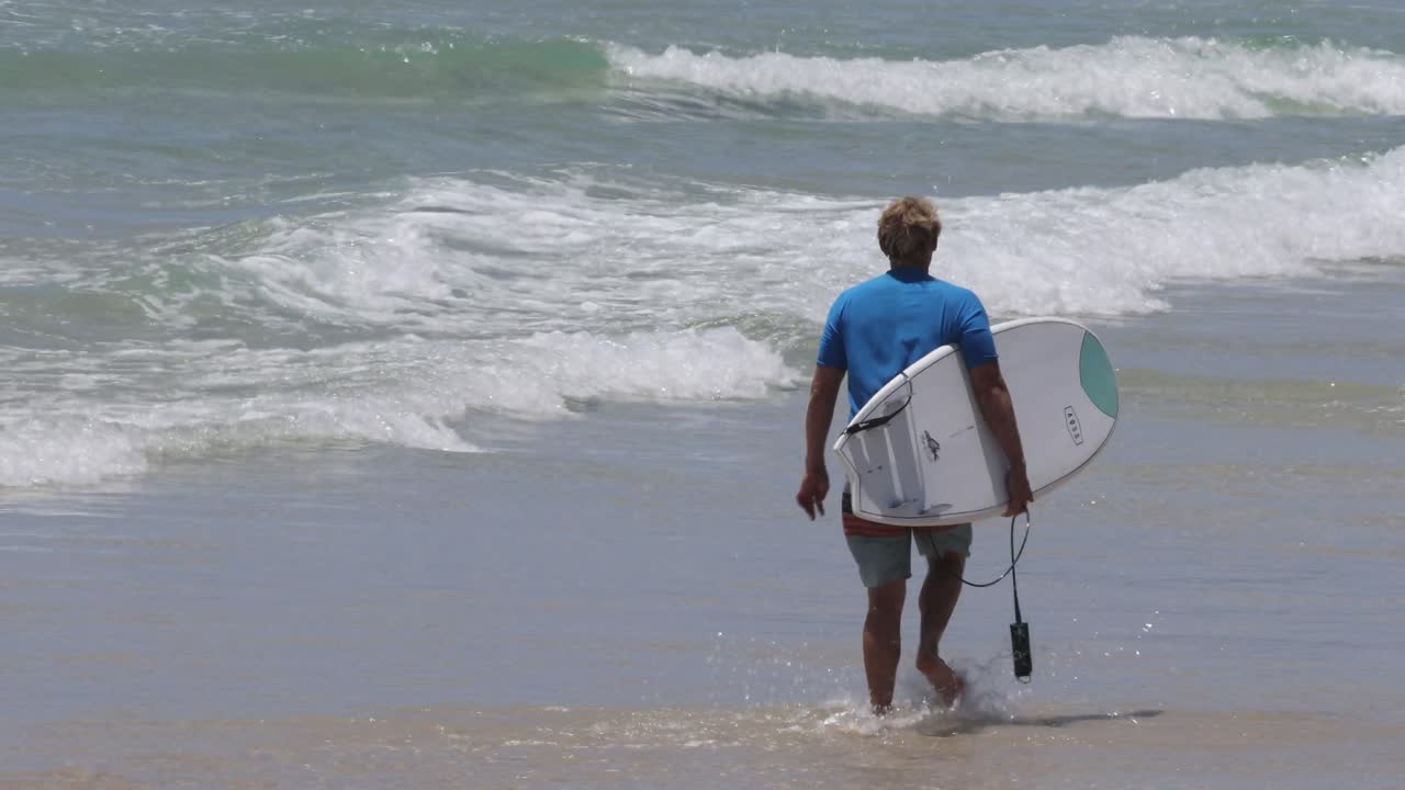 un surfista caminando hacia el mar con una tabla de surf