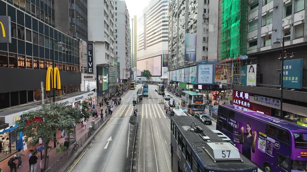 Timelapse street view in Causeway Bay, Hong Kong, featuring trams and buses navigating through heavy traffic with vibrant city life and towering skyscrapers in the background.