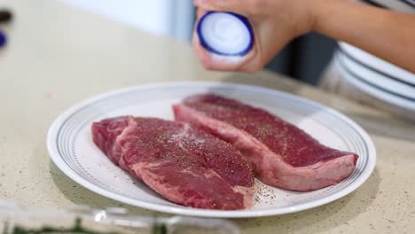 close-up of hands seasoning beef steaks with salt and pepper in a kitchen setting