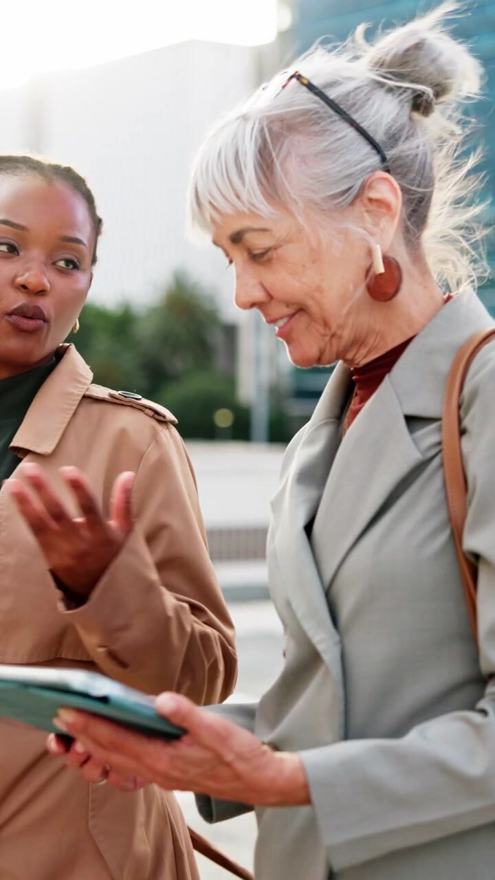 Two Professional Women Discussing Work on a Tablet Outdoors