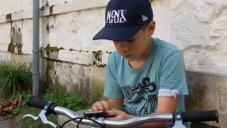 young boy on bicycle focused on his smartphone outdoors
