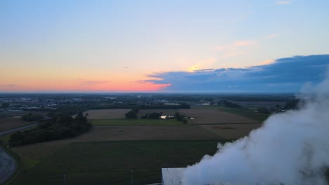 flying backward, revealing steam from a factory during sunset