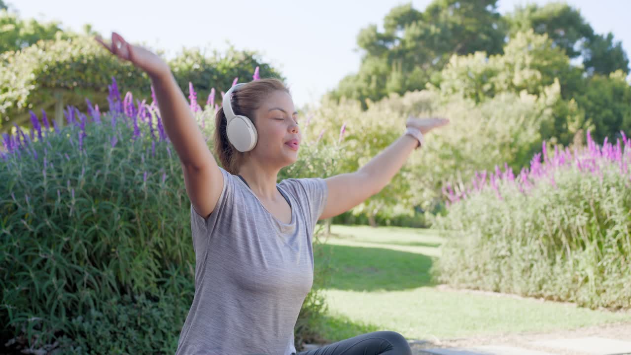 Verticale video: Vrouw past koptelefoon aan en tikt op telefoon, mediterend op een yogamat op een houten vlonder