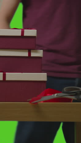 vertical video of man putting down pile of presents in gift wrapped boxes from table shot against green screen 1