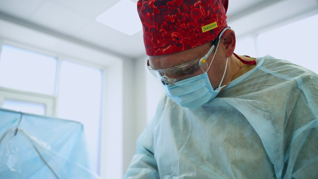 Adult male doctor wearing red hat, mask and glasses for surgery. Portrait of a experienced surgeon busy at operation from low angle view.