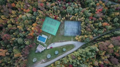 Vista-Aérea-Superior-De-Los-árboles-En-Otoño-Que-Rodean-Las-Instalaciones-Recreativas-Con-Piscina-Al-Aire-Libre-Y-Canchas-De-Tenis-En-Vermont,-EE.UU.