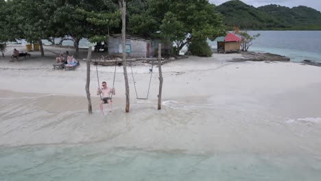 Caucasian-male-tourist-enjoys-beach-swing-on-tiny-sandy-tropical-isle