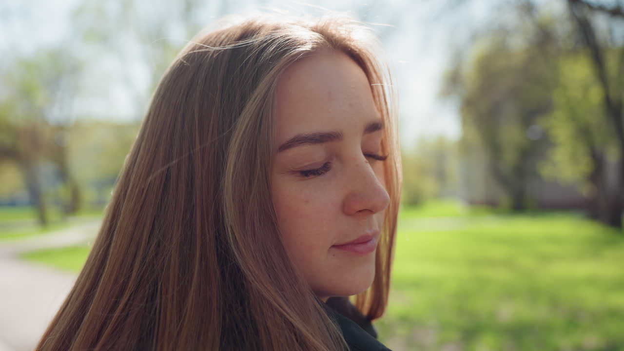Joven caucásica meditando con los ojos cerrados en un parque, expresión de tranquilidad, brisa suave, luz solar entre los árboles, postura relajada, perfil delicado, fondo de césped verde, ambiente contemplativo