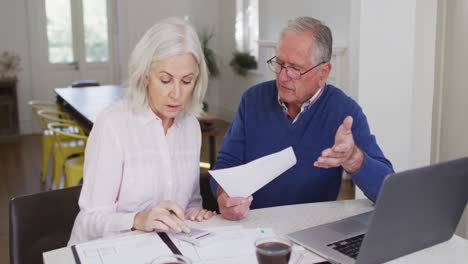 senior couple with laptop using calculator and checking finances at home