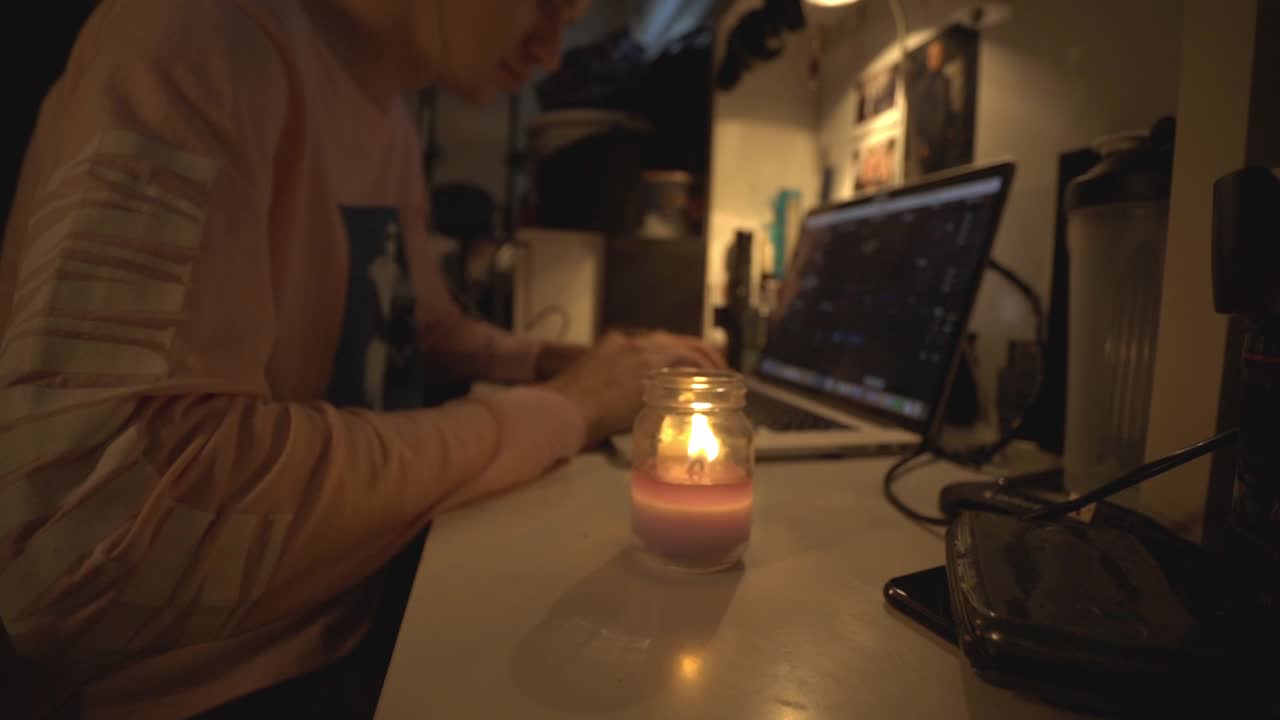 Young Man Sitting And Working On Table With His Laptop And Candle Light. - close up shot