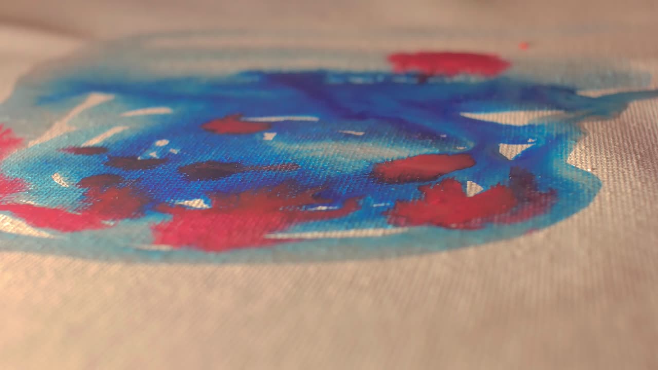 Tampilan makro detail dari cat biru dan oranye yang menyebar di atas kanvas putih. Pengambilan gambar proses artistik ini menyoroti tekstur dan pencampuran warna, sempurna untuk tutorial kreatif dan desain modern.