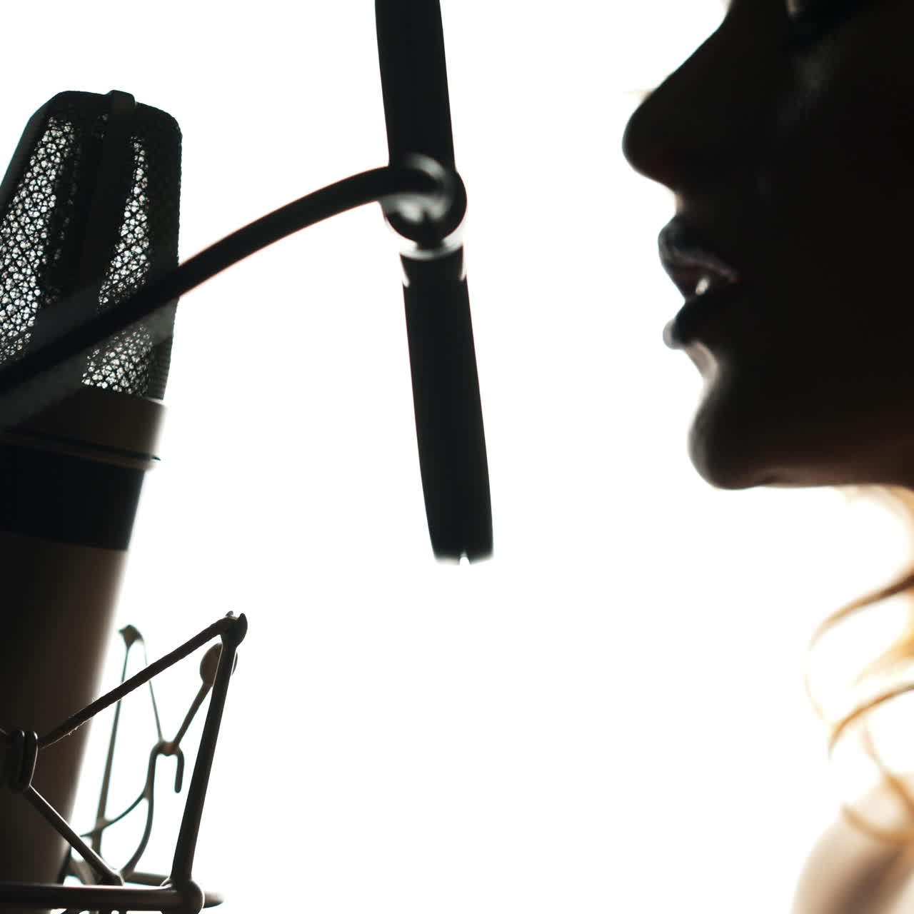 Beautiful woman singing into a microphone in a recording studio. Black and white. Female silhouette Square video