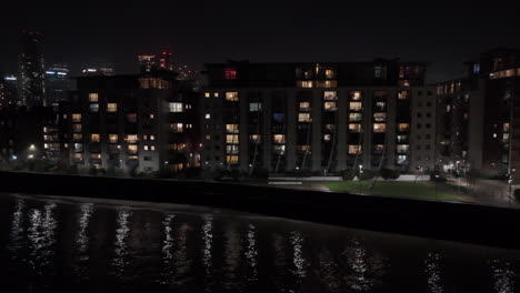 aerial tracking shot of illuminated riverfront apartments, in isle of dogs, london