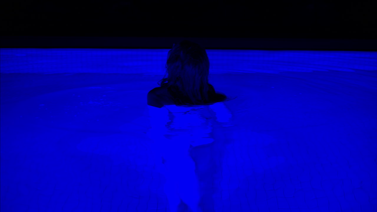 Woman sweeting in a dark blue pool with neon lights at nigh