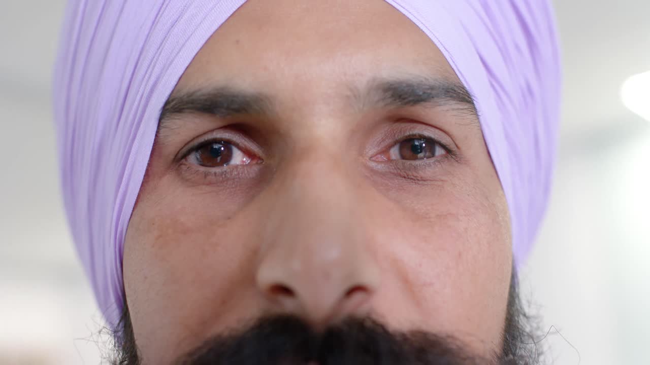 Portrait of happy biracial sikh male doctor in turban looking at camera at hospital, in slow motion