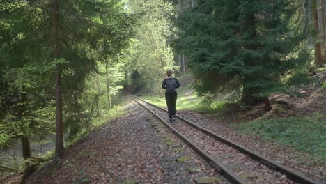 Rear-shot-of-a-tourist-woman-walking-on-railway-track-during-daytime