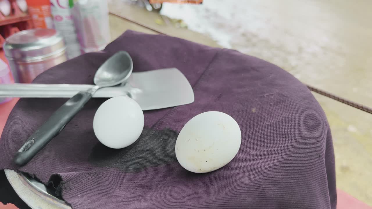 Closeup of two boiled white eggs resting on a dark purple cloth with steam coming out of it