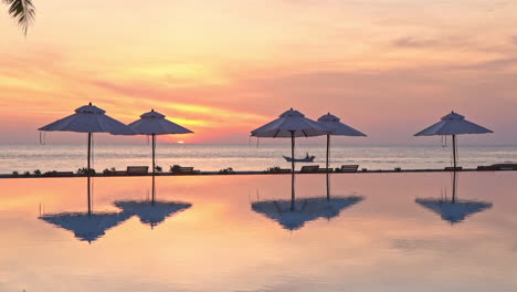 a dramatic orange, yellow and pink sunset reflects in the still waters of a resort swimming pool