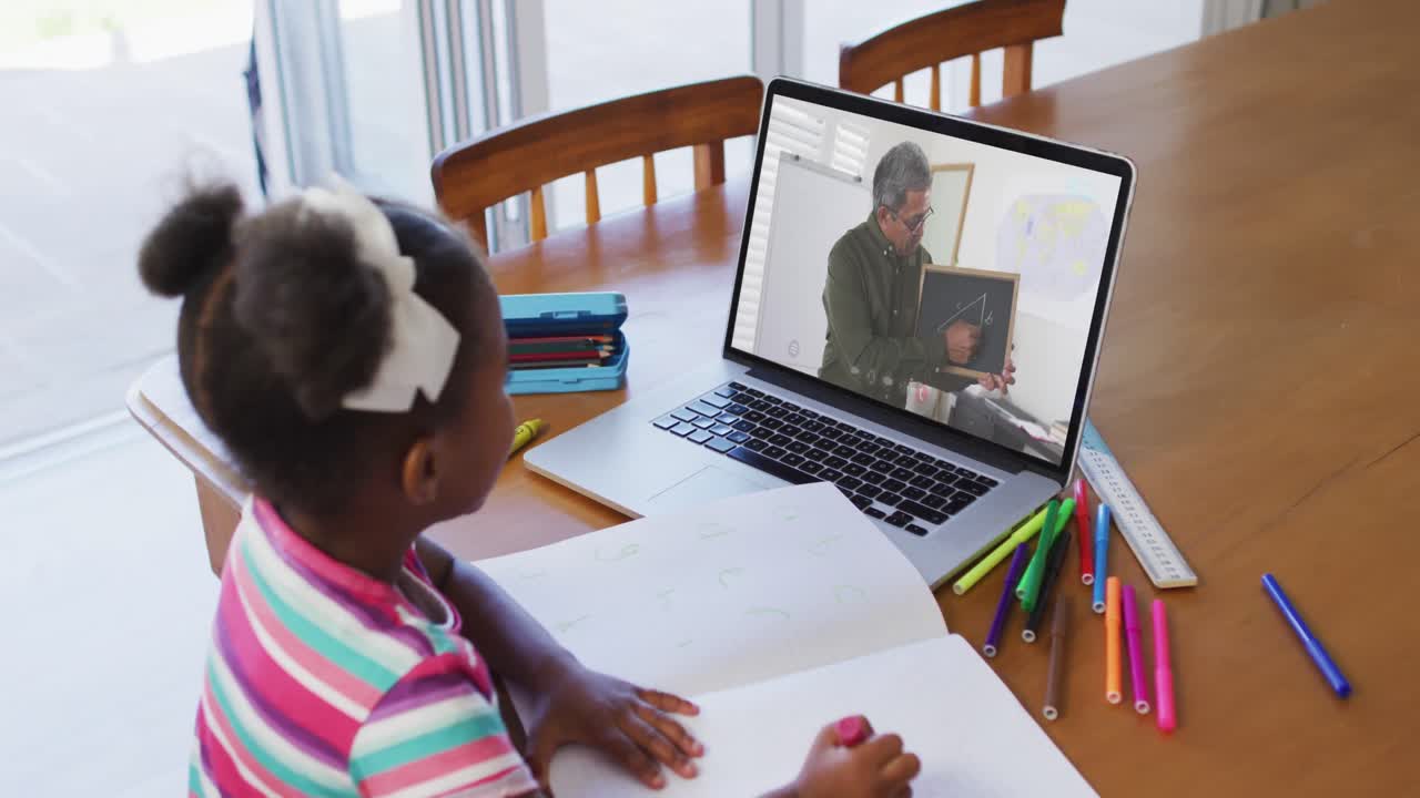 African american girl doing homework while having video call with male teacher on laptop at home