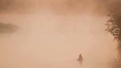 calm lake, river and man fishing from old wooden rowing fishing boat at beautiful misty sunrise in summer morning. fisherman is in wooden boat. russian nature