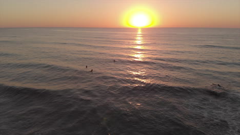 surfers in the sea during sunset in algarve, portugal - surfing at golden hour - aerial drone, arc shot