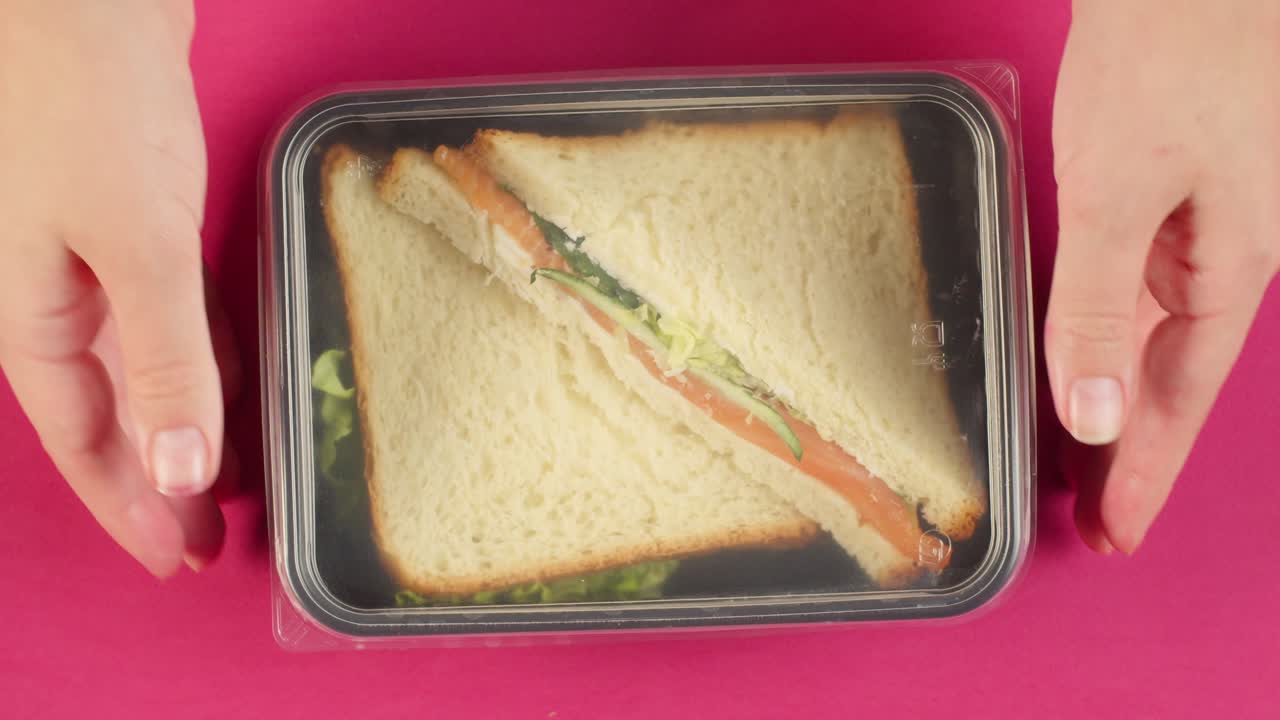 Hænder lukker og tager en laksesandwich i en plastikbeholder