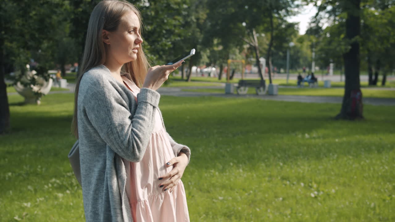 Pregnant woman using phone in a park