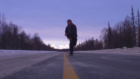 skater skates through a snowy street with mountan views behind him