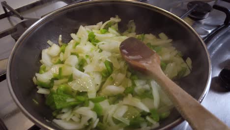 cebolla humeante y pimiento verde en sartén con cuchara de madera, cámara lenta acercándose