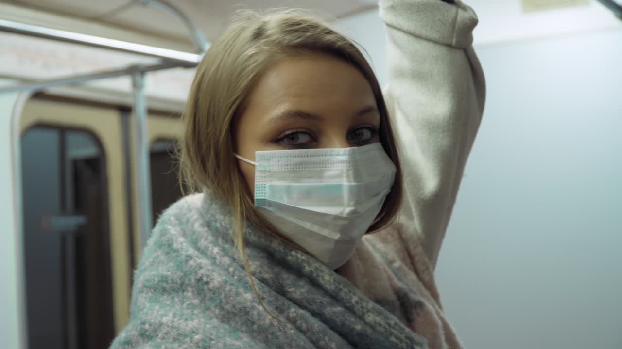 девушка в медицинской маске смотрит на камеру в транспорте