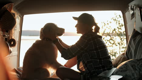 Mujer-Acariciando-A-Un-Perro-En-Una-Furgoneta-Al-Atardecer-A-Orillas-Del-Lago