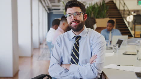 Retrato-De-Un-Hombre-De-Negocios-En-Una-Oficina-Moderna-Con-Colegas-Reunidos-Alrededor-De-Una-Mesa-En-Segundo-Plano