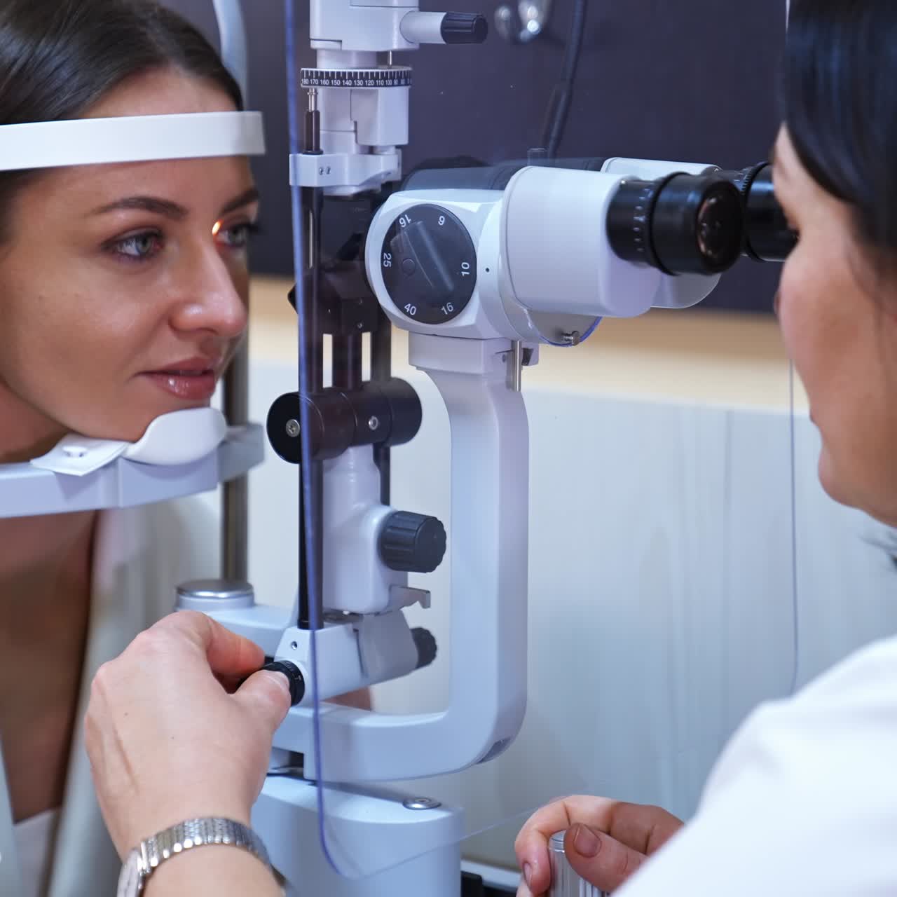 Attractive long-haired woman at optician's check up. Doctor uses special equipment to check the eyesight of a patient