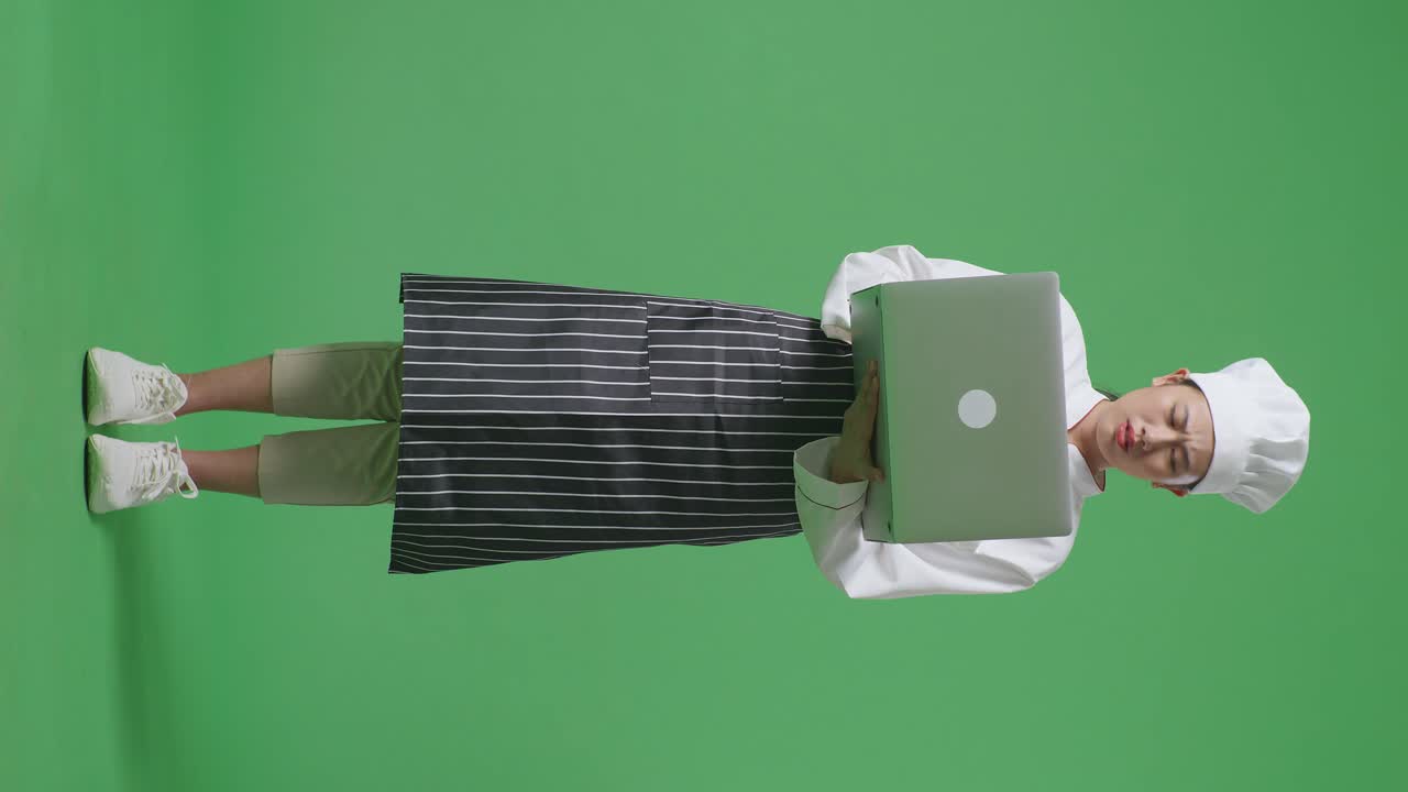 Full Body Of Asian Woman Chef Using A Laptop And Having A Headache While Standing In The Green Screen Background Studio