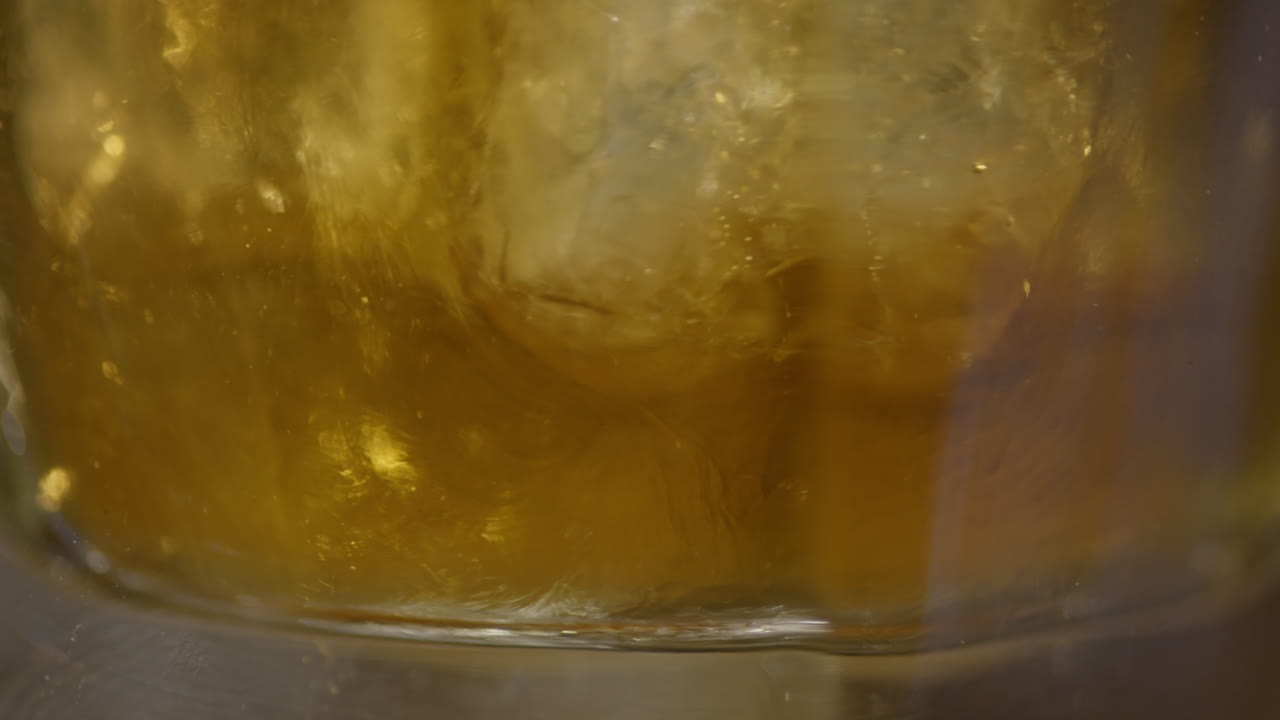 Primo piano di whisky nel bicchiere con cubetti di ghiaccio, movimento lento