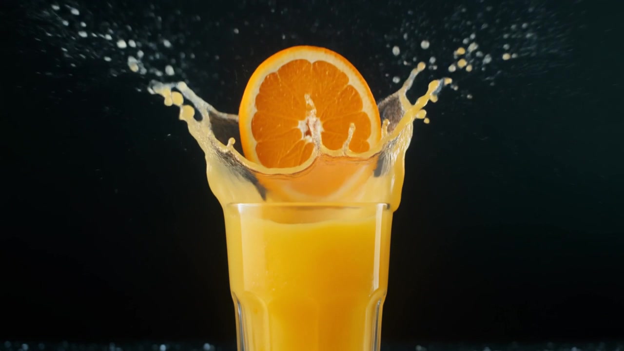 Orange Slice Falling into a Glass of Fresh Orange Juice