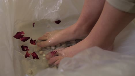 woman stepping barefoot in water bucket with petals slow motion, spa pampering