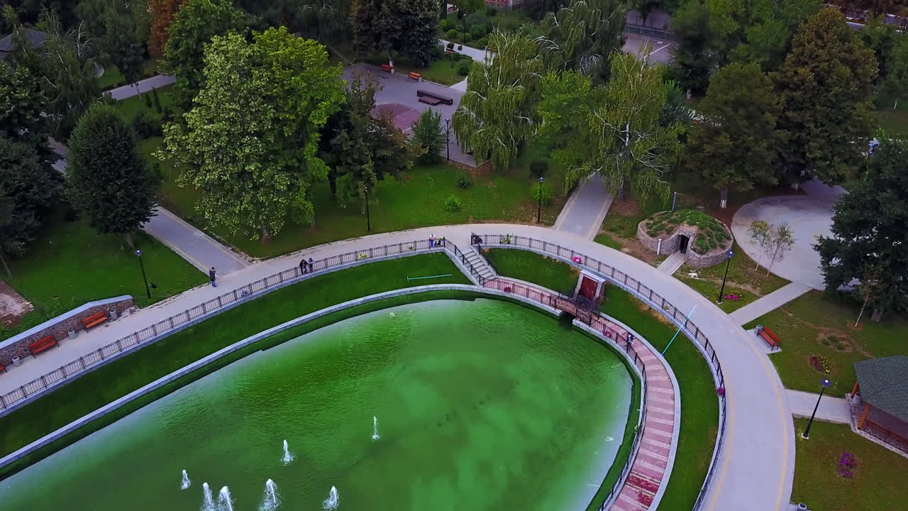 Artificial oval pond with group of fountains in the middle. Beautiful park in the city. Top view.